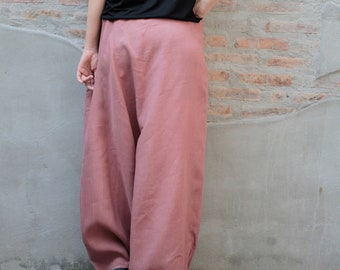 May include: A person wearing a black short-sleeved top and dusty rose-colored wide-leg pants. The pants have a loose, flowing design. The person is standing in front of a weathered brick and concrete wall.