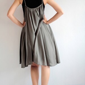 May include: A grey sleeveless dress with a loose, flowing fit. The dress has a scoop neck and a slightly gathered skirt.