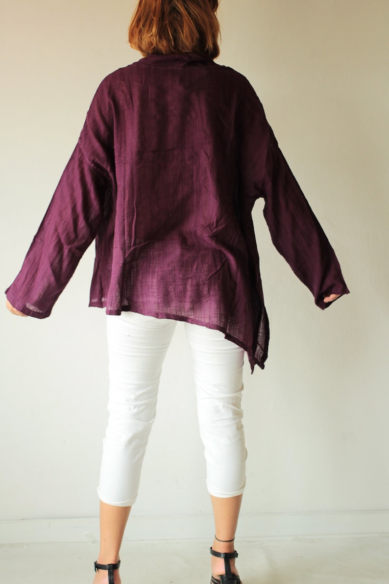 May include: A long-sleeved, loose-fitting, purple shirt with a slightly asymmetrical hemline. The shirt is made of a soft, lightweight fabric and has a relaxed fit.