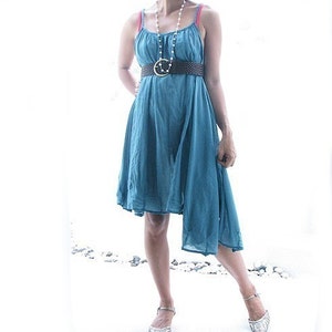 May include: A teal blue sleeveless dress with a brown belt and a pearl necklace. The dress has a high neckline and a flowing skirt.