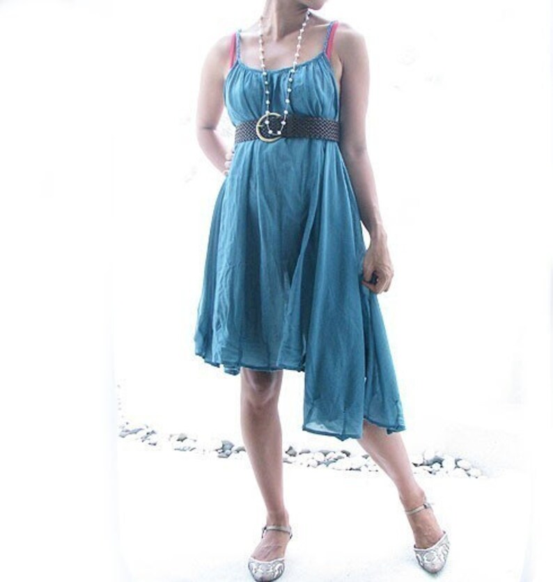 May include: A teal blue sleeveless dress with a brown belt and a pearl necklace. The dress has a high neckline and a flowing skirt.