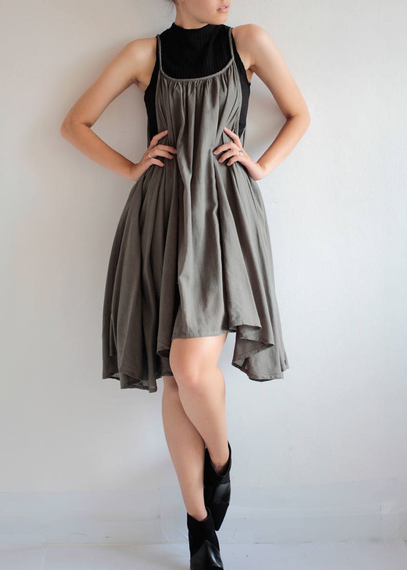 May include: A grey sleeveless dress with a gathered neckline and a flowing, asymmetrical hemline. The dress is worn with a black turtleneck top and black ankle boots.