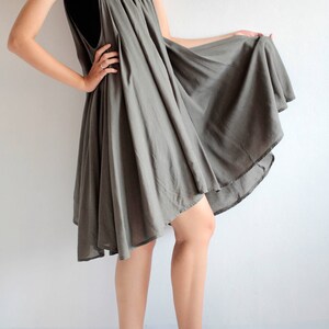 May include: A grey, flowing, asymmetrical dress with a scoop neck and thin straps. The dress is made of a lightweight fabric and has a relaxed fit. The model is wearing black ankle boots.