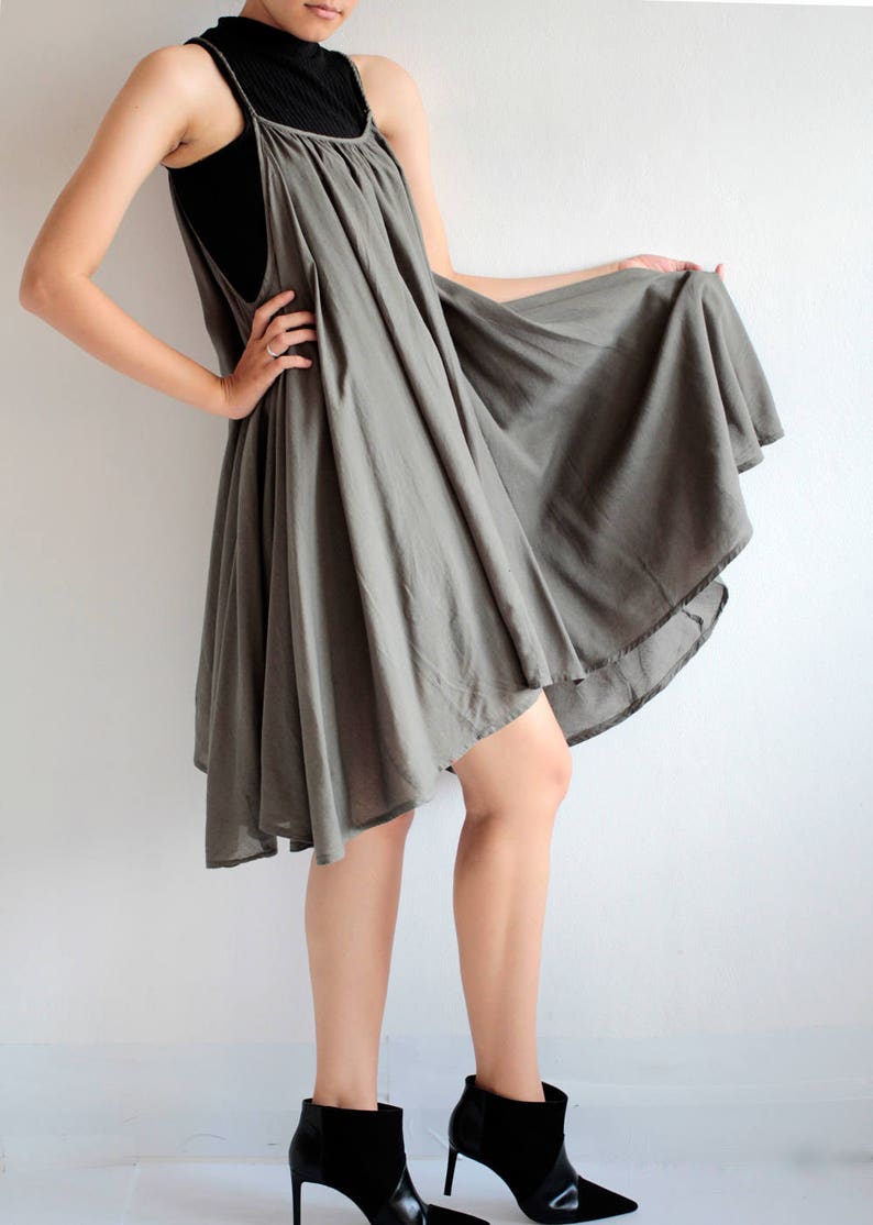 May include: A grey, flowing, asymmetrical dress with a scoop neck and thin straps. The dress is made of a lightweight fabric and has a relaxed fit. The model is wearing black ankle boots.