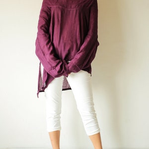 May include: A woman is wearing a loose-fitting, off-the-shoulder, purple top with white cropped pants and black heeled sandals.