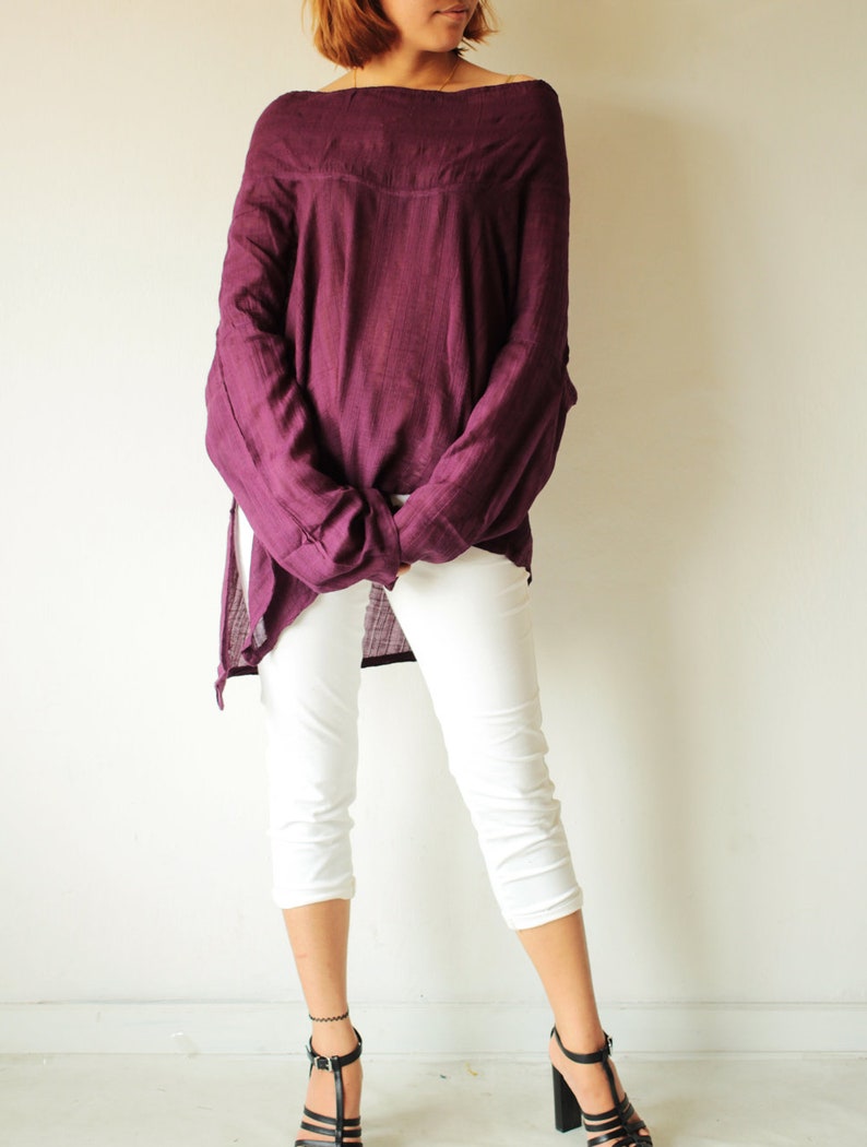 May include: A woman is wearing a loose-fitting, off-the-shoulder, purple top with white cropped pants and black heeled sandals.