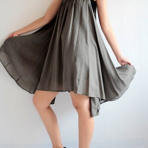 May include: A grey sleeveless dress with a loose, flowing fit. The dress has a high neckline and a slightly asymmetrical hemline. The model is wearing black ankle boots.