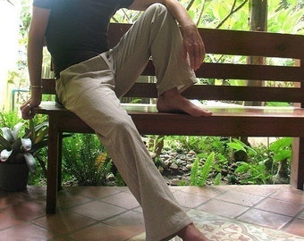 May include: Tan linen pants with a brown t-shirt. The person is sitting on a wooden bench outdoors. The pants are a light neutral color, and the t-shirt is a darker brown. The setting includes greenery and a tiled floor.