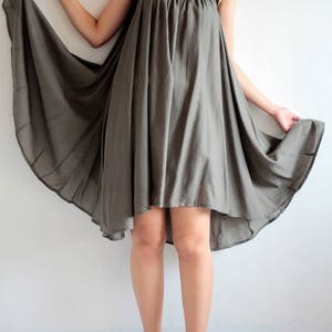 May include: A grey, flowing, sleeveless dress with a high neckline and a slightly longer back hemline. The dress is made of a soft, lightweight fabric and has a relaxed fit.