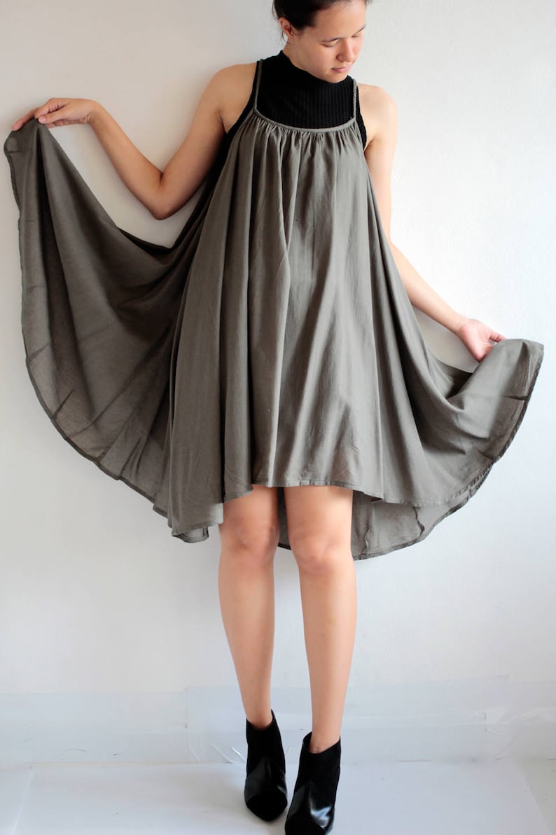 May include: A grey, flowing, sleeveless dress with a high neckline and a slightly longer back hemline. The dress is made of a soft, lightweight fabric and has a relaxed fit.