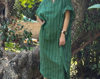 May include: A woman wearing a green and white striped dress with a v-neck and short sleeves. She is standing in front of a tree.