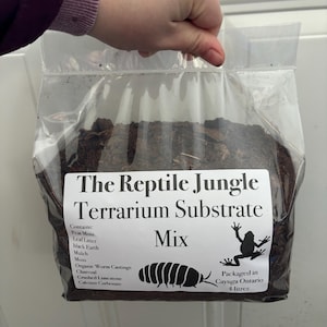 Peut inclure: Un sac en plastique transparent rempli de substrat de terrarium brun. Le sac porte une étiquette blanche sur laquelle est inscrit "The Reptile Jungle Terrarium Substrate Mix" et qui liste les ingrédients : tourbe de mousse, litière de feuilles, terre noire, paillis, mousse, fumier de vers organique, charbon de bois, calcaire concassé, carbonate de calcium. L'étiquette indique également "Emballé à Cayuga Ontario 4 Litres".
