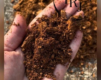May include: A close-up of a hand holding a quantity of brown reptile substrate, possibly wood chips. The material is coarse and textured. The image includes a logo that says "THE REPTILE JUNGLE" in a circle.