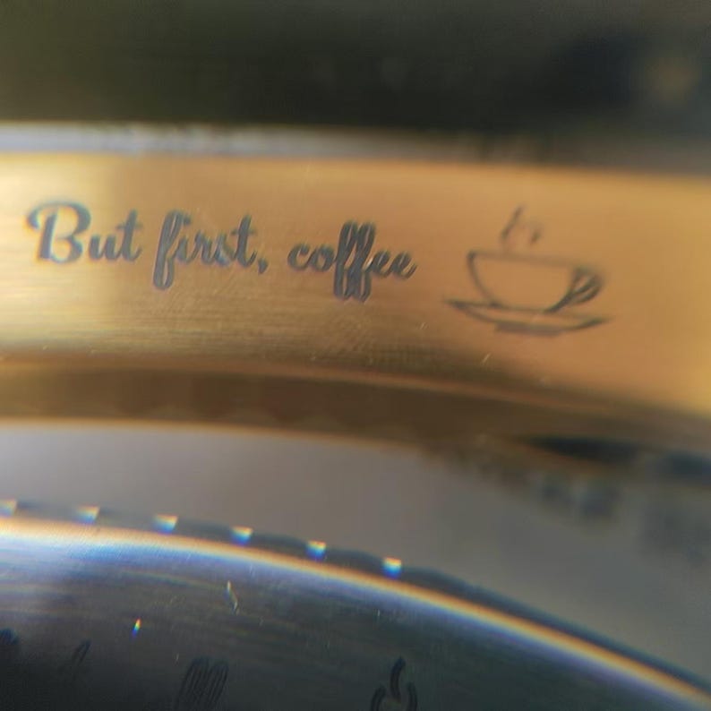 May include: Gold-colored metal band with the engraved text "But first, coffee" and a small coffee cup icon.