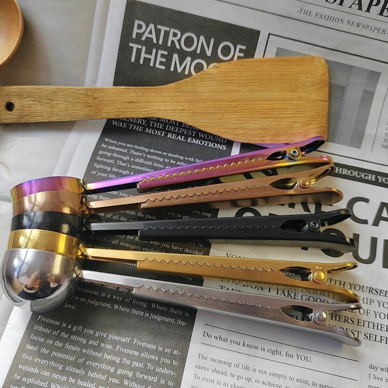 May include: A set of six colorful metal hair clips with a zig-zag pattern on the edge. The clips are arranged in a stack, with the largest clip at the bottom and the smallest clip at the top. The clips are made of different metals, including gold, silver, and black.