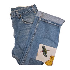 May include: A pair of blue denim jeans with a butterfly and flower design patch on one leg.