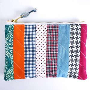 May include: A colourful patchwork zippered pouch with a variety of patterns, including gingham, polka dots and paisley. The pouch is made of fabric and has a gold zipper.