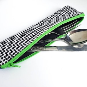 May include: A black and white patterned zippered pouch with a green zipper. The pouch contains a fork, spoon, and knife.