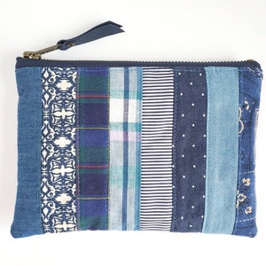 May include: A blue patchwork zippered pouch with a variety of blue and white patterns. The pouch is made from recycled denim and other fabrics.