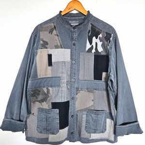 Peut inclure: Une chemise à manches longues grise avec un motif patchwork composé de différentes nuances de gris, de noir et de motifs camouflage. La chemise a une fermeture boutonnée à l'avant, un col et deux poches. L'étiquette sur la chemise indique "WindRiver".