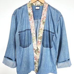 May include: A blue denim jacket with a floral print lining. The jacket has a collar and long sleeves. The label on the jacket reads "Jool".