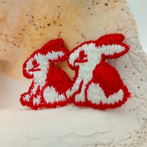 May include: Two red embroidered bunny rabbit patches with white outlines. The bunnies are facing each other and are in a sitting position.
