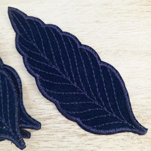 May include: A dark blue felt leaf applique with a detailed stitched design. The leaf is perfect for adding a touch of nature to crafts and projects.