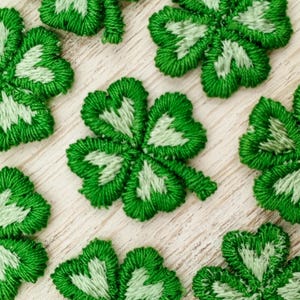 May include: A collection of eight green felt four-leaf clover patches. The clovers are embroidered with a white center and have a slightly raised texture.