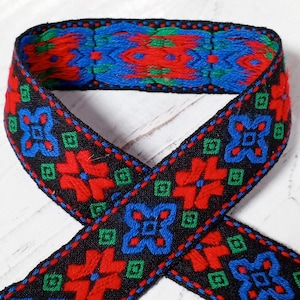 May include: Black woven ribbon with a repeating pattern of red, blue, and green geometric shapes. The ribbon is folded in half, showing the pattern on both sides.