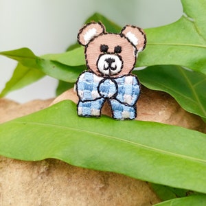 May include: A brown embroidered teddy bear wearing a blue and white checkered bow tie.