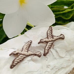 May include: Two brown embroidered bird appliques with beige stitching. The appliques are on a white background.