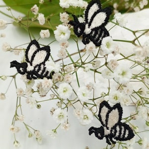 May include: Two black and white embroidered bee patches on a white background with small white flowers.