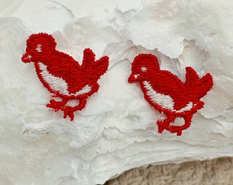 May include: Two red embroidered bird appliques with white accents. The birds are facing opposite directions and have a simple design.