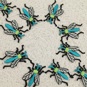 May include: Ten embroidered iron-on patches of blue and green mosquitos. The mosquitos are black with white wings and have a green body and blue legs.