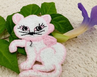 May include: White embroidered cat applique with pink accents. The cat has black eyes and a pink nose. The applique is perfect for adding a touch of whimsy to any project.