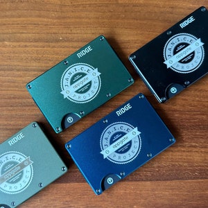 May include: Four Ridge wallets with a green, blue, and black color scheme. Each wallet has the text "J.A.N.I.C.E. PROJECT" and "appgate" printed on the front.
