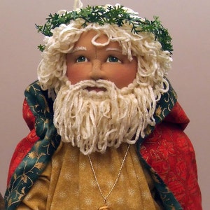 May include: A handmade doll dressed as a Christmas character. The doll has a white beard and a green wreath on its head. The doll is wearing a red and green robe with gold accents. The doll is holding a gold cross.