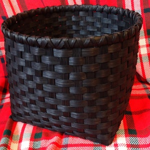 May include: A black woven basket with a square base and a rounded top. The basket is made of a dark, natural material and has a tightly woven pattern.