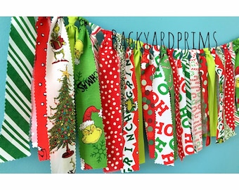 Op de afbeelding: Een kerstbanner met rode en groene stofstroken met verschillende feestelijke patronen, waaronder een Grinch, een kerstboom en de woorden "Oh Ho" en "Grinch". De banner is gelabeld met "Backyard Prims".