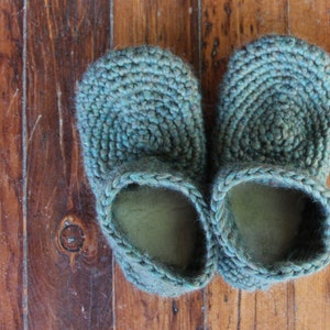 May include: A pair of teal blue crocheted slippers. The slippers are made with a thick yarn and have a simple, classic design.