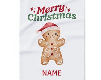 Puede incluir: Una manta blanca con temática navideña con un hombre de jengibre de acuarela con un gorro de Papá Noel. Las palabras "Merry Christmas" están en rojo y verde encima del hombre de jengibre, con la palabra "NAME" en rojo debajo.