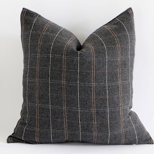 Op de afbeelding: Een vierkant decoratief kussen met een donkergrijs ruitpatroon. Het kussen heeft een rasterontwerp met dunne witte en bruine lijnen. Het kussen is gemaakt van een zachte stof en is geschikt voor een woonkamer of slaapkamer.