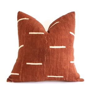 Puede incluir: Una almohada de color óxido con un patrón geométrico blanco. La almohada está hecha de una tela suave y texturizada.