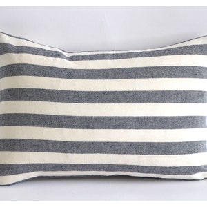 Puede incluir: Una funda de cojín a rayas blancas y grises. La funda de cojín está hecha de un tejido suave y tejido y tiene una forma rectangular.