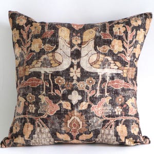 May include: Square throw pillow with a vintage-style design. The pillow features a dark brown background with a repeating pattern of birds, flowers, and foliage in shades of beige, peach, and gold. The pillow is approximately 18 inches square.