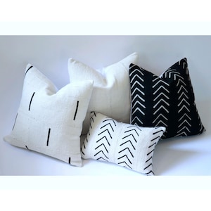 Puede incluir: Cuatro almohadas decorativas con patrones geométricos en blanco y negro. Las almohadas están hechas de tela blanca con costuras negras y están dispuestas sobre una superficie blanca.