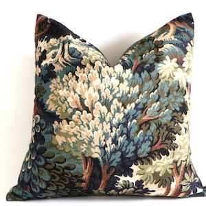 May include: Square decorative pillow with a detailed tree and foliage pattern. The pillow features a tapestry-like design with shades of blue, green, beige, and brown. The pillow is a square shape and is likely used for home decor.