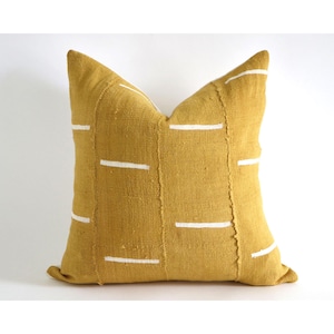 May include: A mustard yellow throw pillow with white geometric lines. The pillow is made of a textured fabric and has a simple, modern design.