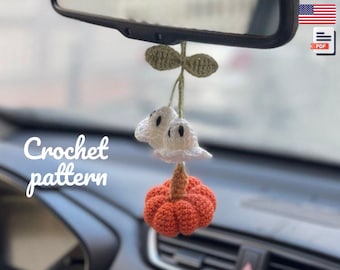 May include: A handmade crochet car charm featuring a white ghost and an orange pumpkin. The charm is suspended from a green stem with leaves. The words "Crochet pattern" are written in white script.