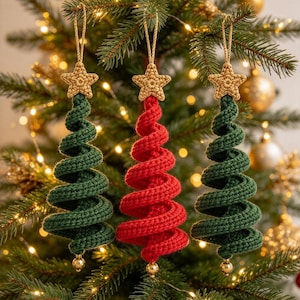 Könnte beinhalten: Drei spiralförmige Häkel-Weihnachtsbaumschmuckstücke, die an goldenen Schnüren hängen. Zwei Anhänger sind dunkelgrün und einer ist rot, jeweils gekrönt von einem kleinen beigen Häkelstern und einer goldenen Perle an der unteren Spitze.